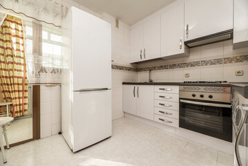 Kitchen with white furniture, a large solitary refrigerator and access to a drying terrace