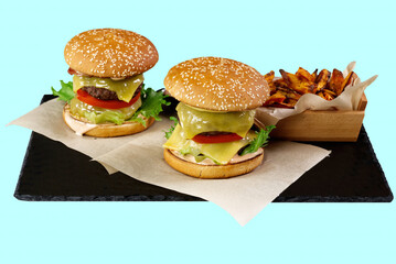 two Big burgers and sweet potato isolated on black stone plate. light blue background. close up