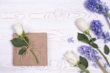 Spring composition, A gift box wrapped in craft paper and blue hyacinth flowers, white roses on a white table top. Flat lay. Copy space for text