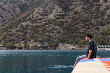 Fototapeta na wymiar Barefooted young man sitting on colorful dock. He is happy. He puts his feet in sea.