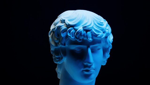 Plaster head sculpture Apollonian in blue neon light close-up. Gypsum ancient statue isolated on black background.