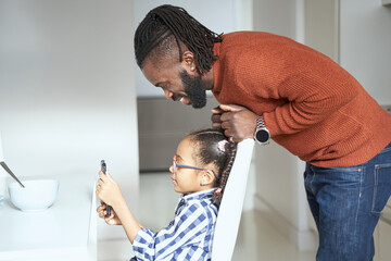 Young girl sitting on chair and looking at mobile phone with father