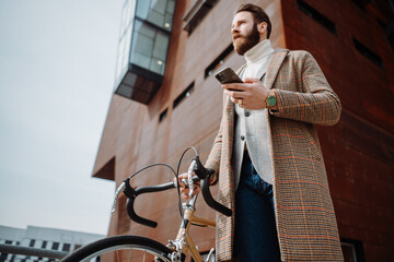 Young man with bicycle holding a smartphone front of building. Creative businessman in a modern business area.