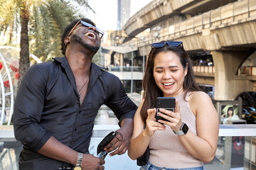 Multiracial friends laughing and using the mobile next to a mall