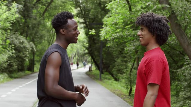 Two African Ameican Guys Bumping Elbows, Talking And Laughing Outdoors