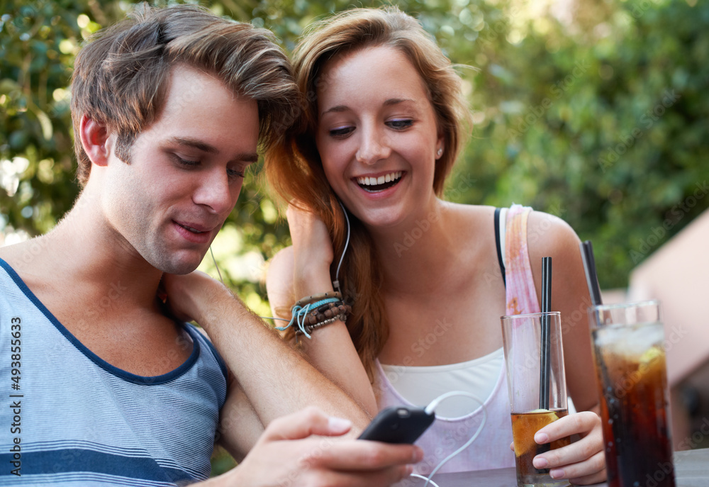 Wall mural Socialising in the twenty first century. Cute teen couple sharing an MP3 player and listening to music while enjoying their beverages.