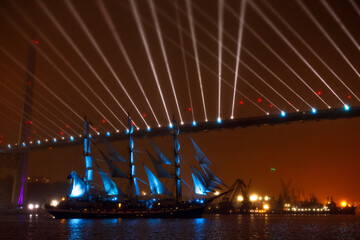 A beautiful sailing ship passes under the glowing Golden Bridge in Vladivostok. Training sailboat...