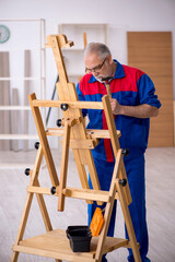 Old male carpenter repairing drawing easel