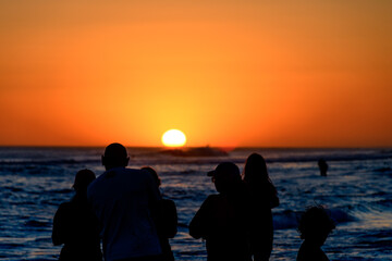 Silhouettes of people in front of a colorful sunset on the beach.