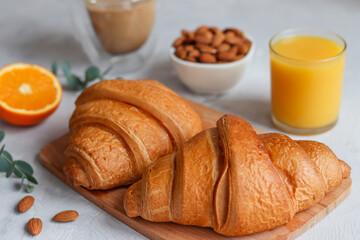 Two croissants with orange juice, orange fruit, coffee and almond nuts on the table. Delicious french or continental breakfast. Selective focus, close-up