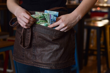 Server using pockets of her apron to keep cash money tips