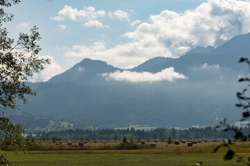 hay bales on the field under a bright sky with white clouds and Alp mountains in the background in a cozy rural countryside on a sunny day