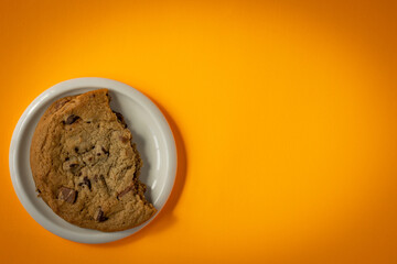 Broken chocolate chip cookie on a saucer surrounded by circular gradient from orange to yellow background