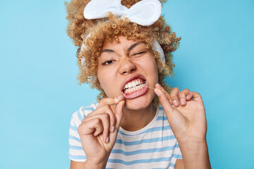 Young beautiful woman with curly combed hair uses dental floss for cleaning teeth wears headband...