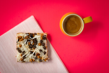 Cup of espresso on red background next to slice of pastry placed on piece of parchment paper