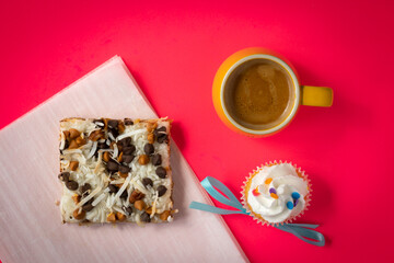 Cup of espresso coffee, slice of pastry and a cupcake on bright red background.