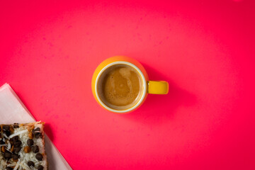 Cup of espresso next to pastry slice on pink background.