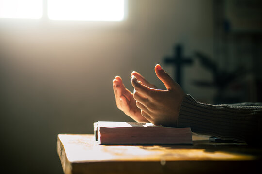 Christian hands praying on holy bible in light of morning at wooden table. christian concept.