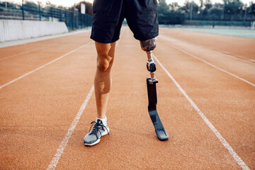 Sportsman with artificial leg standing on running track at stadium. Legs on running track. - Powered by Adobe