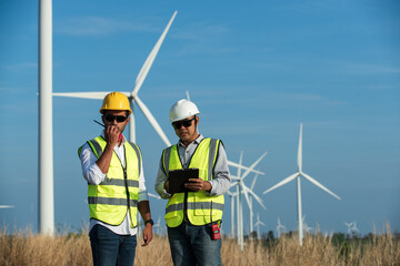 portrait of a worker in a hardhat. Two maintenance engineer  in hand holding tablet and radio communication in wind turbine farm on background. 