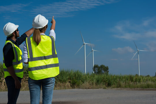 Back View Of Two Engineers Discussing Against Turbines On Wind Turbine Farm.