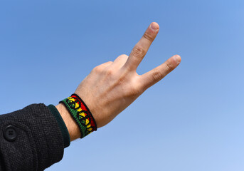 Handmade DIY friendship bracelet with Rasta flag pattern with a peace symbol on male wrist on sky...