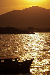 Photograph of the silhouette of a small boat with people on board on a beach in the late afternoon. Reflections of the sun are reflected in the waters of the sea.