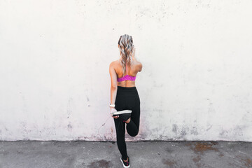 Fototapeta premium young active sport woman stretching quads on a wall. Home backyard workout. Copy space.