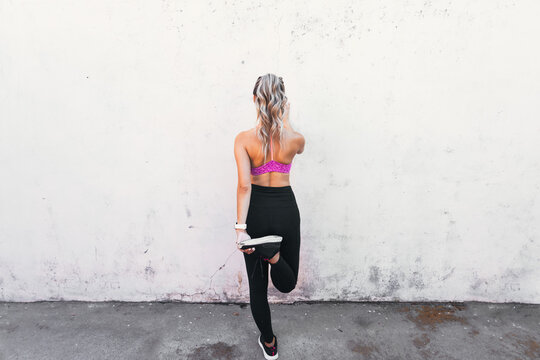 young active sport woman stretching quads on a wall. Home backyard workout. Copy space.