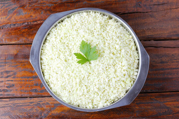 raw homemade cauliflower rice in stainless bowl over rustic wooden table