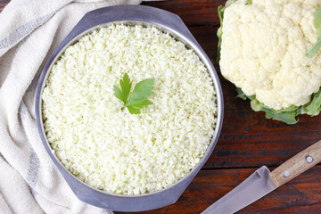 raw homemade cauliflower rice in stainless bowl over rustic wooden table