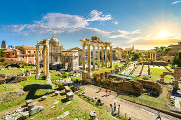 Fototapeta premium The ancient Roman Forum with the sun setting above the Colosseum in the historic center of Rome, Italy. View facing northeast from above the Portico Dii Consentes.