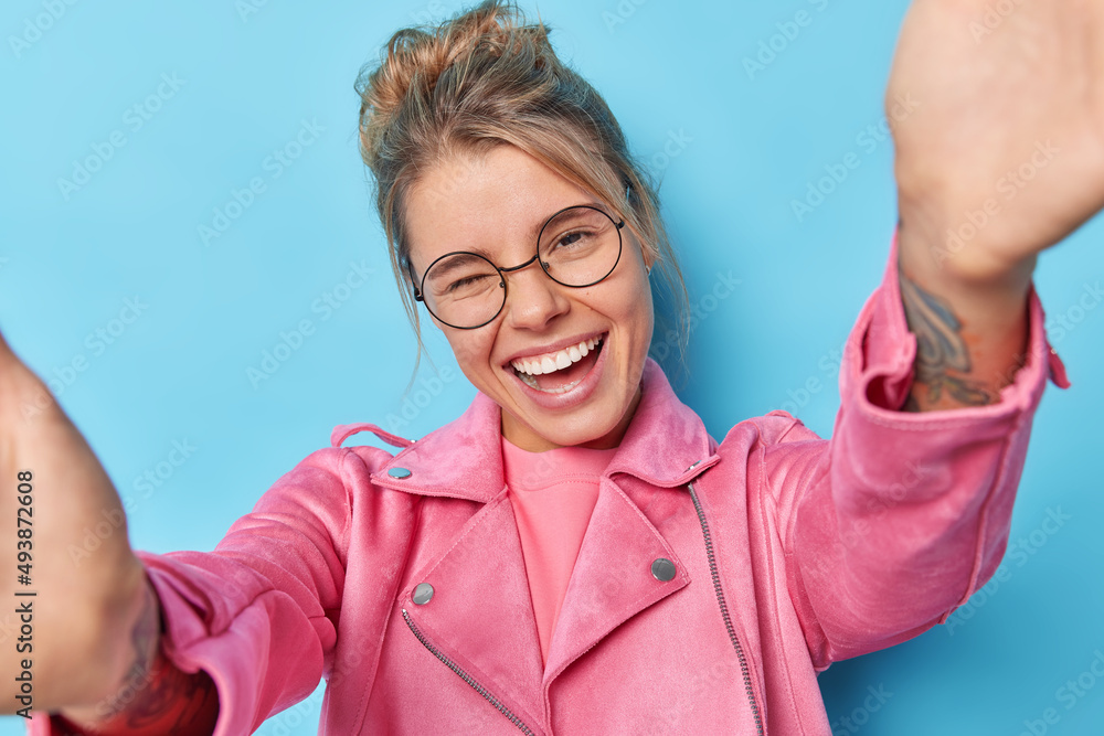 Wall mural positive young woman smiles broadly winks eye has fun keeps arms outstretchs poses for selfie foolis - Wall murals
