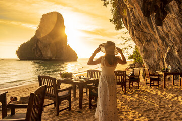 Woman tourist in white dress dinner in restaurant cave on Phra nang Beach at sunset, Railay, Krabi,...