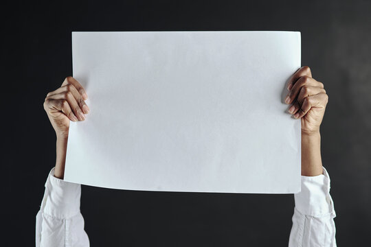 Take A Look Here. Shot Of Hands Holding Up A Blank Page Against A Dark Background.