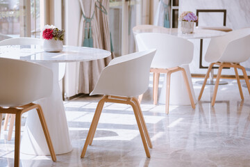 Fototapeta na wymiar Sunlight streamed through floor-to-ceiling windows into a reception room set with white tables. White minimalist modern dining room interior design.