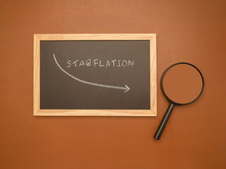 Hand draws an arrow of stagflation with chalk on a blackboard and magnifying glass over a brown...