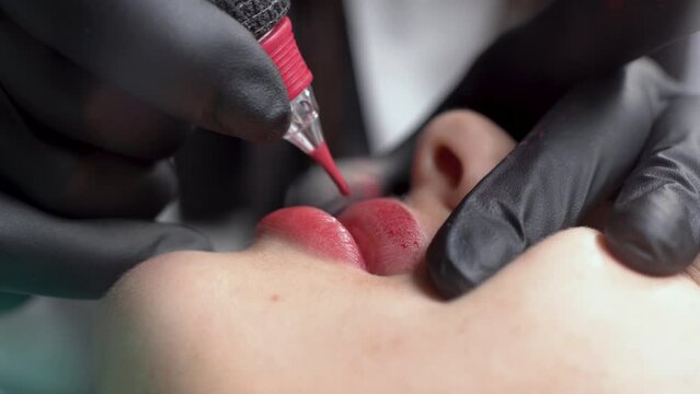 lip tattoo microblading in a permanent makeup clinic, applying coloring pigment to lips using a tattoo machine, makeup pigmentation on a woman's face close-up. Macro