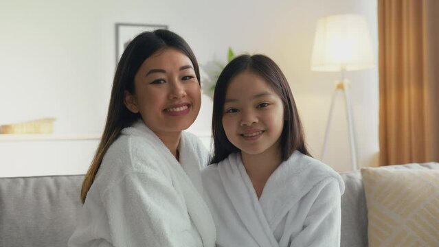 Portrait of happy asian mother and daughter smiling to camera and rubbing noses, sitting together at home, zoom in
