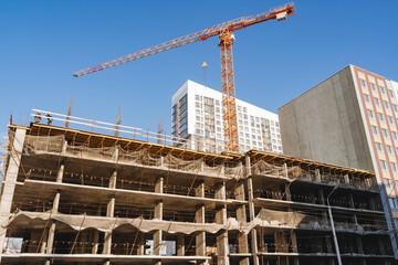 Construction site. A crane builds a house. The crane performs work lifting cargo, concrete slabs, floor slabs.