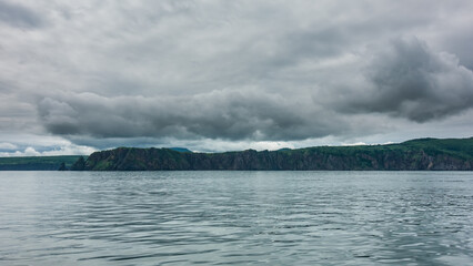 Kamchatka coast against the sky. Gray clouds hang over the rocky slopes. Ripples on the water of the Pacific Ocean. Avacha Bay