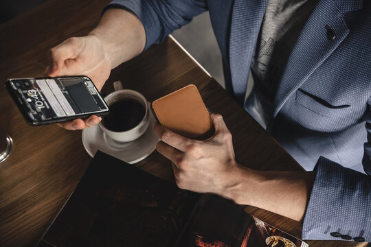 A Business Man Is Sitting At A Table In A Cafe Holding A Mobile Phone And Waiting For A Bill For Breakfast And Coffee. Top View, Horizontal Orientation, Copy Space