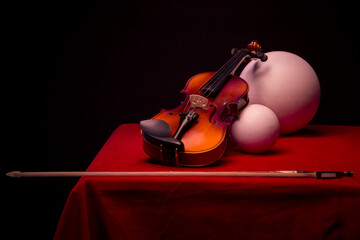 Still life with a violin, balls and bow on the red table
