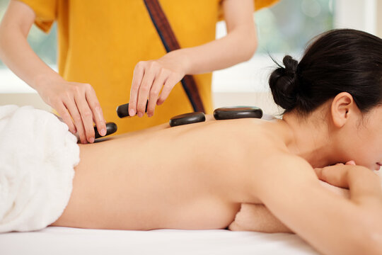 Beautician putting hot basalt stones along spine of female client