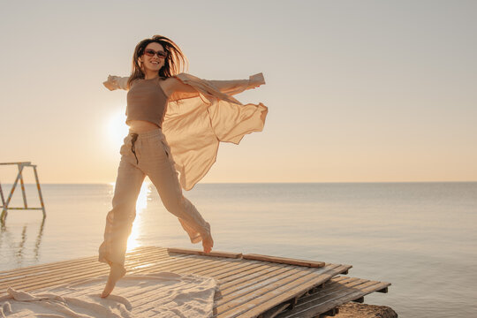 Bottom view of happy caucasian young girl admiring sunrise or sunset on tropical beach. Brown-haired woman in sunglasses is having fun. Nice vacation by the sea.