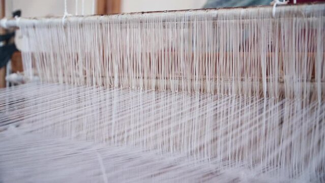 Industrial antique weaving machine with many white threads operated by person, close up view