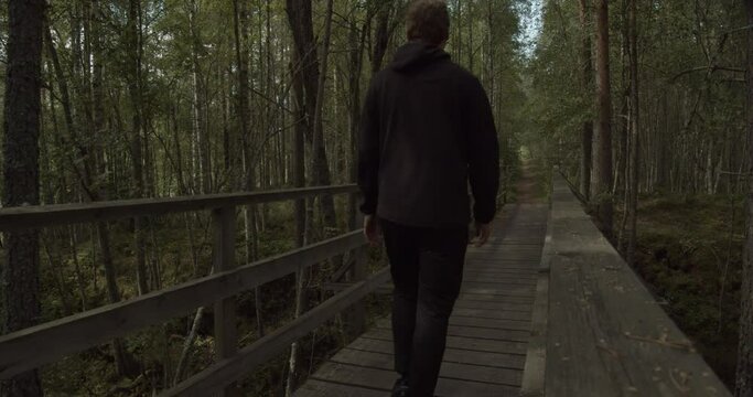 Man walks over a bridge in a dark forrest in Sweden