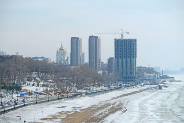Fototapeta premium Magadan, Russia - 03.24.2018 : The bank of the frozen Amur River on the background of administrative buildings.