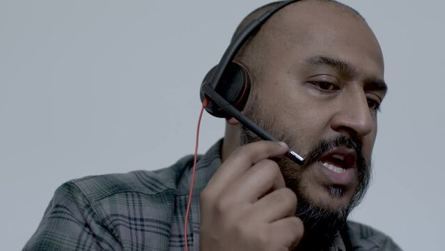 A close up shot of the face of an Asian call centre representative, the man attempting to take a call but experiences technical issues with the audio on his headset microphone working from home
