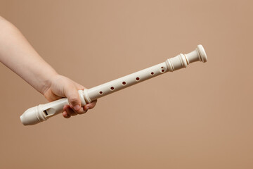 Hold ivory color common fipple flute with one hand closeup, beige background. Woodwind musical...
